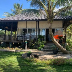 Traditional Balinese beachfront villa with black-trimmed veranda, signature orange egg chair, and lush palm grove surroundings